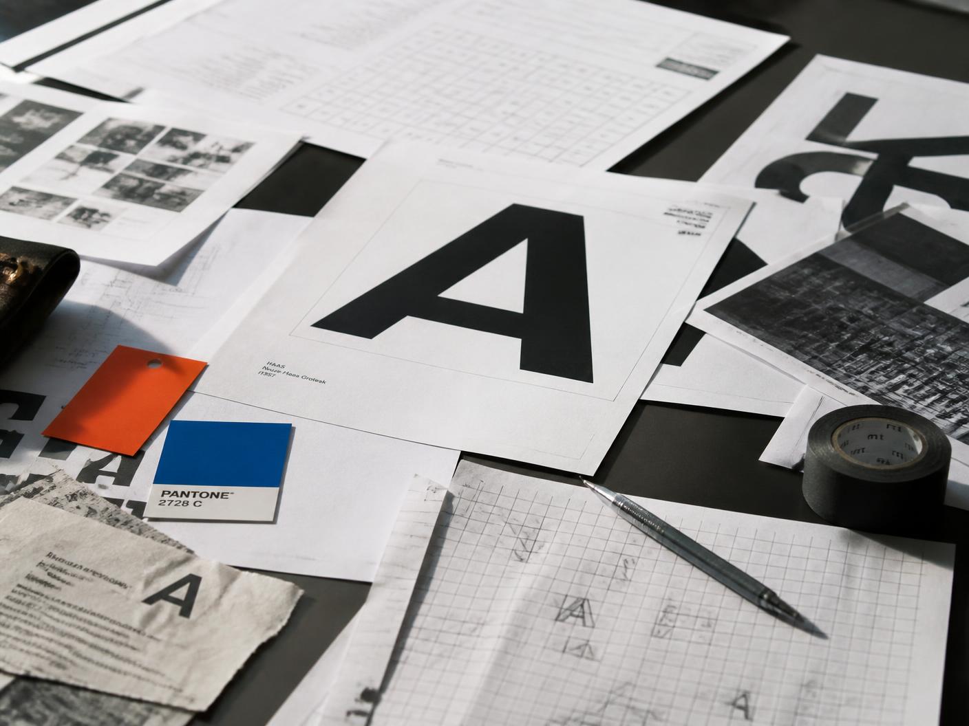 Loose pencil sketches, type proofs and a marked-up brief spread across a studio table