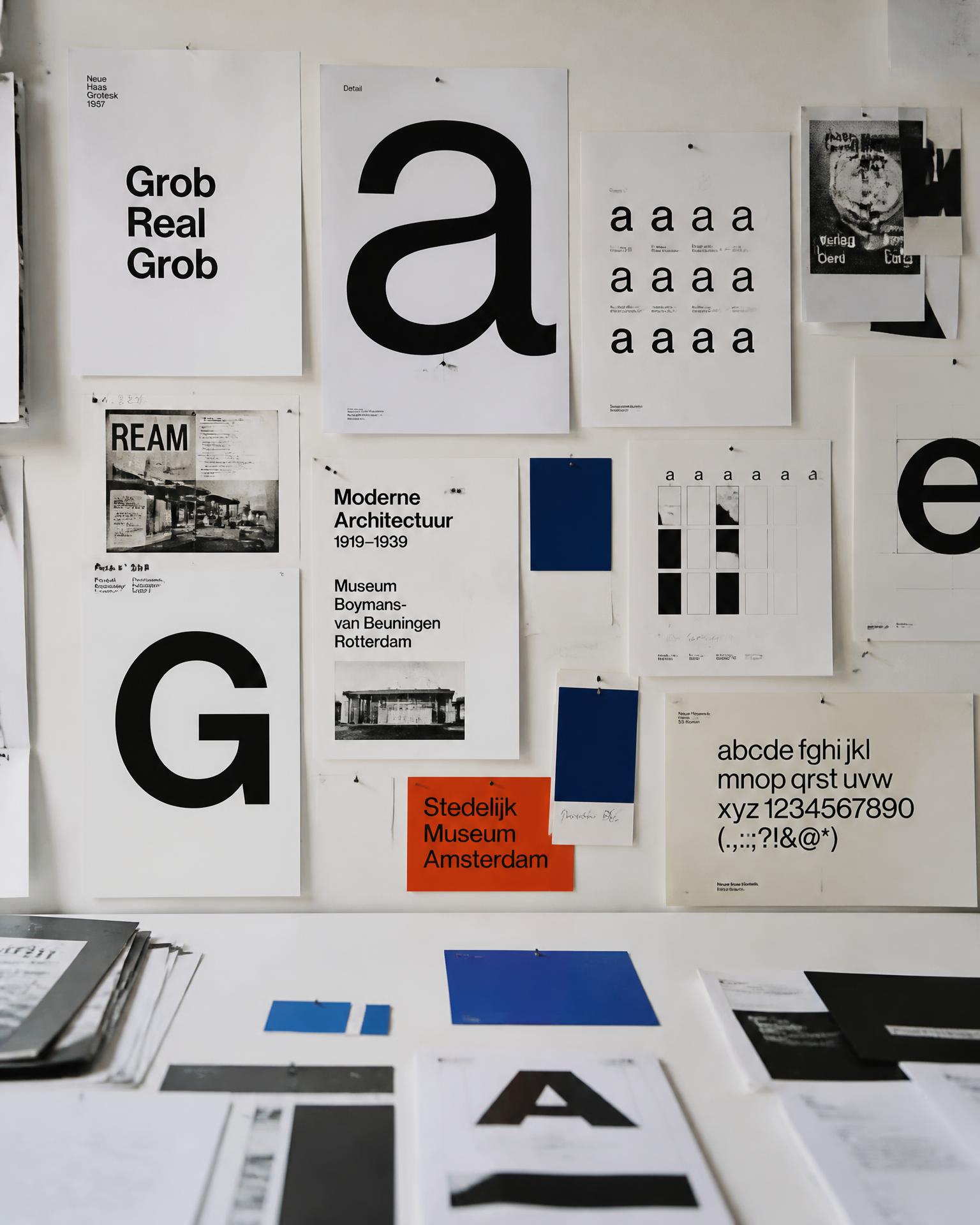 Type specimens, printed references and colour swatches pinned above a studio table, annotated in pencil