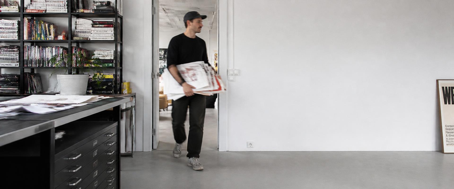A designer walking through the studio carrying a stack of printed proofs